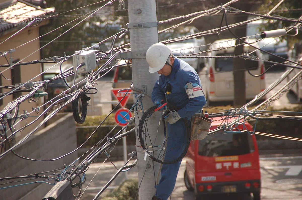 Line technician working on overhead cable fittings at a utility pole