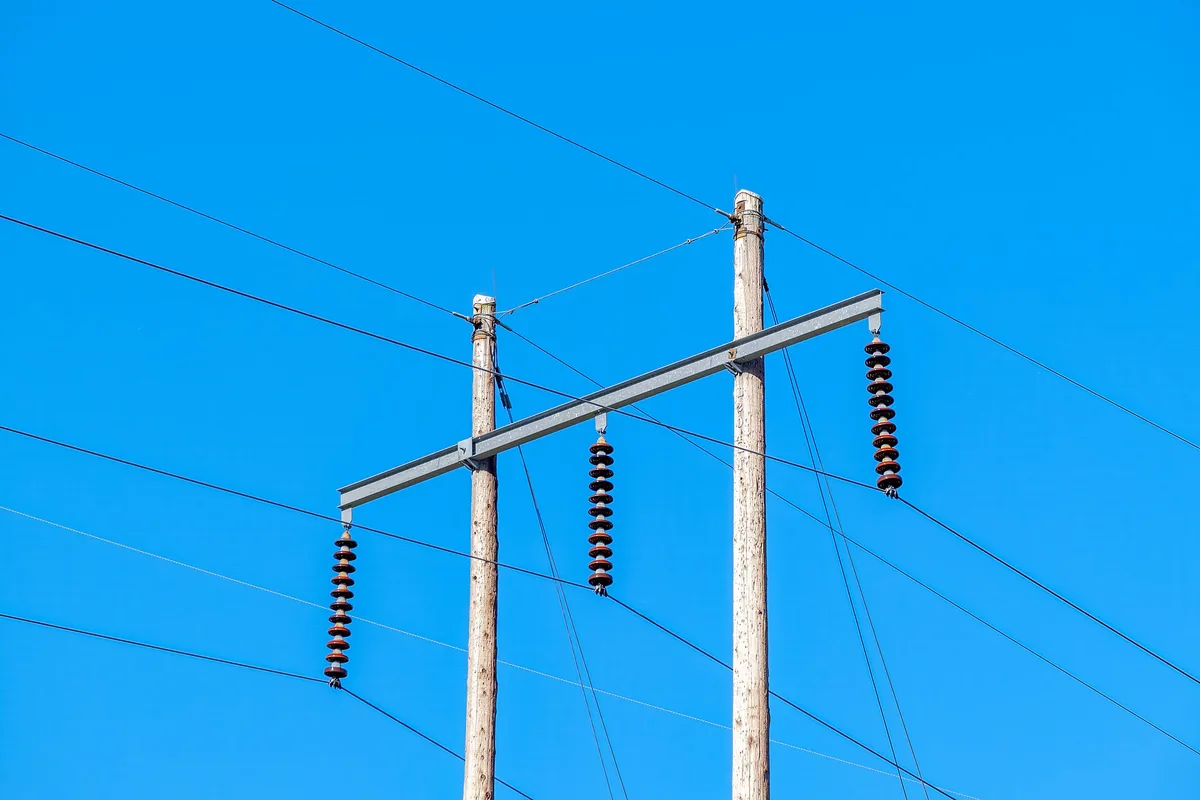 Galvanized steel crossarm bolted between wood utility poles with suspension insulators