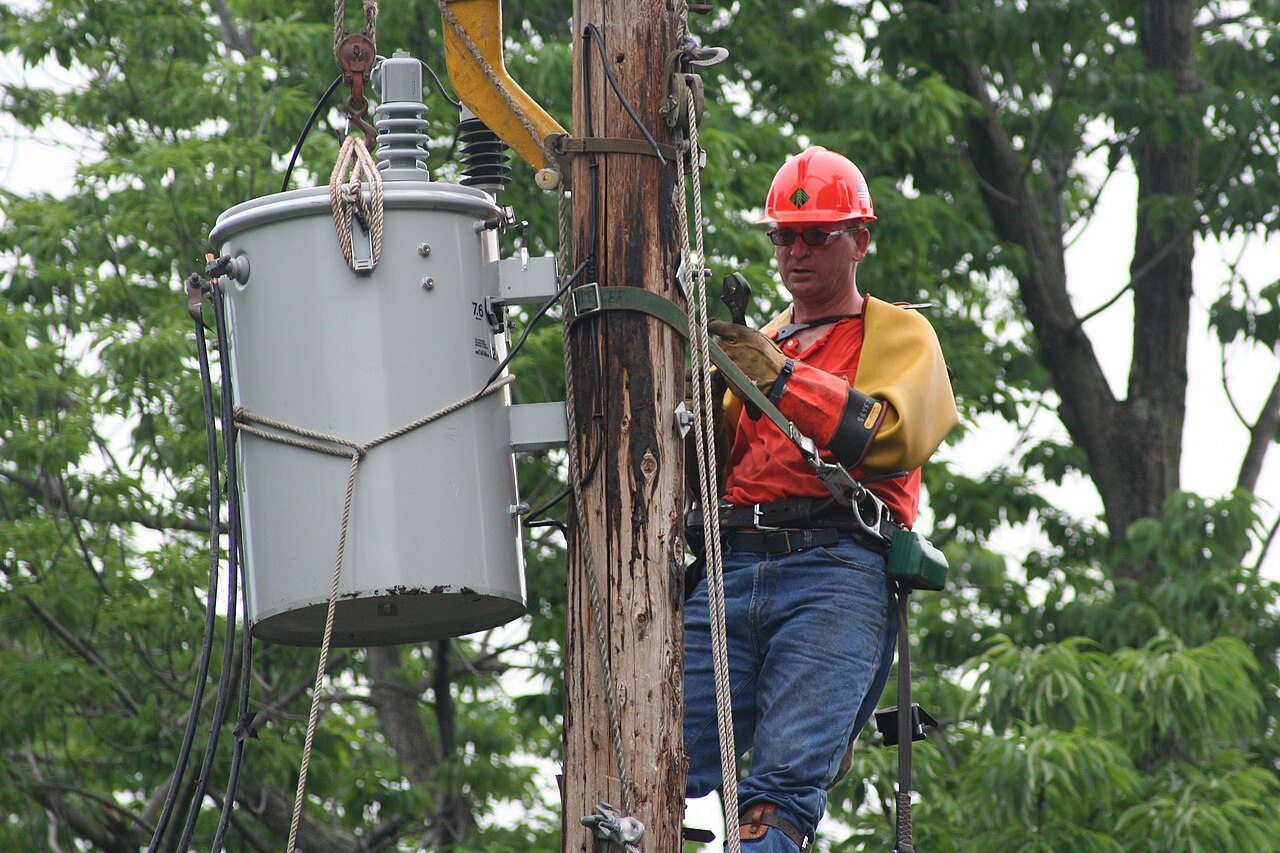 Lineman in protective equipment working on overhead line hardware at a pole