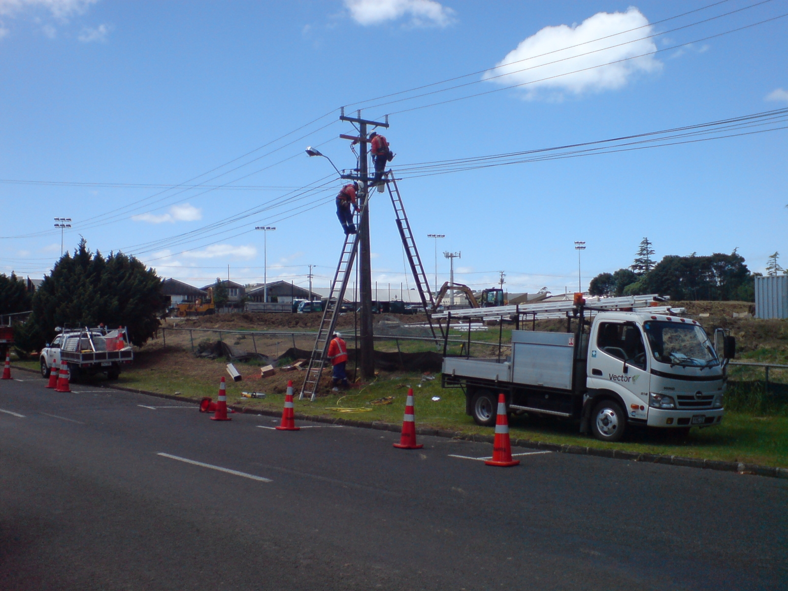 Linemen working on distribution pole hardware from ladders
