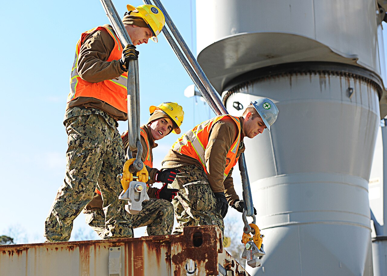Workers checking rigging on loaded equipment before shipment