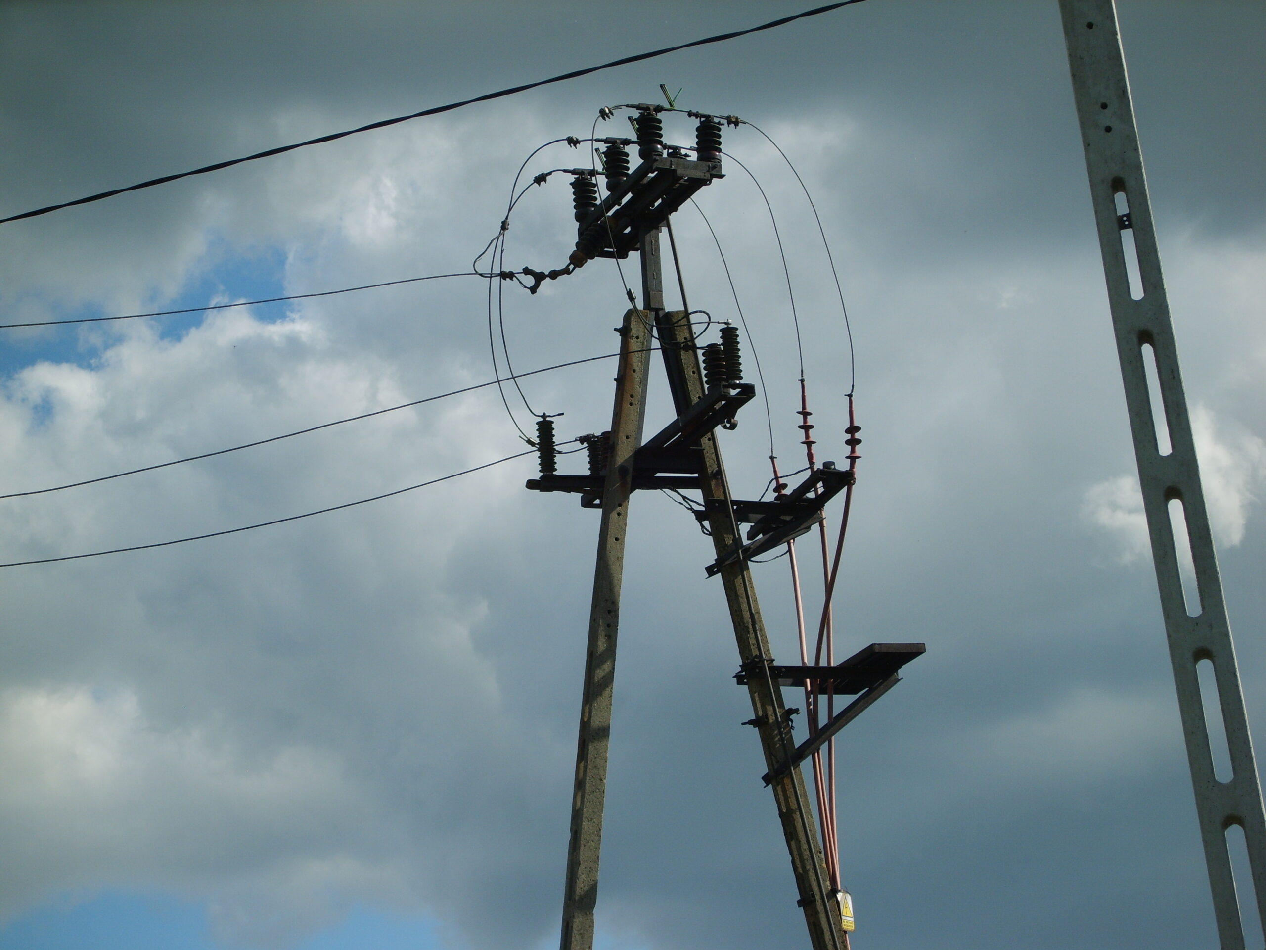 Concrete distribution pole carrying line insulators under a cloudy sky