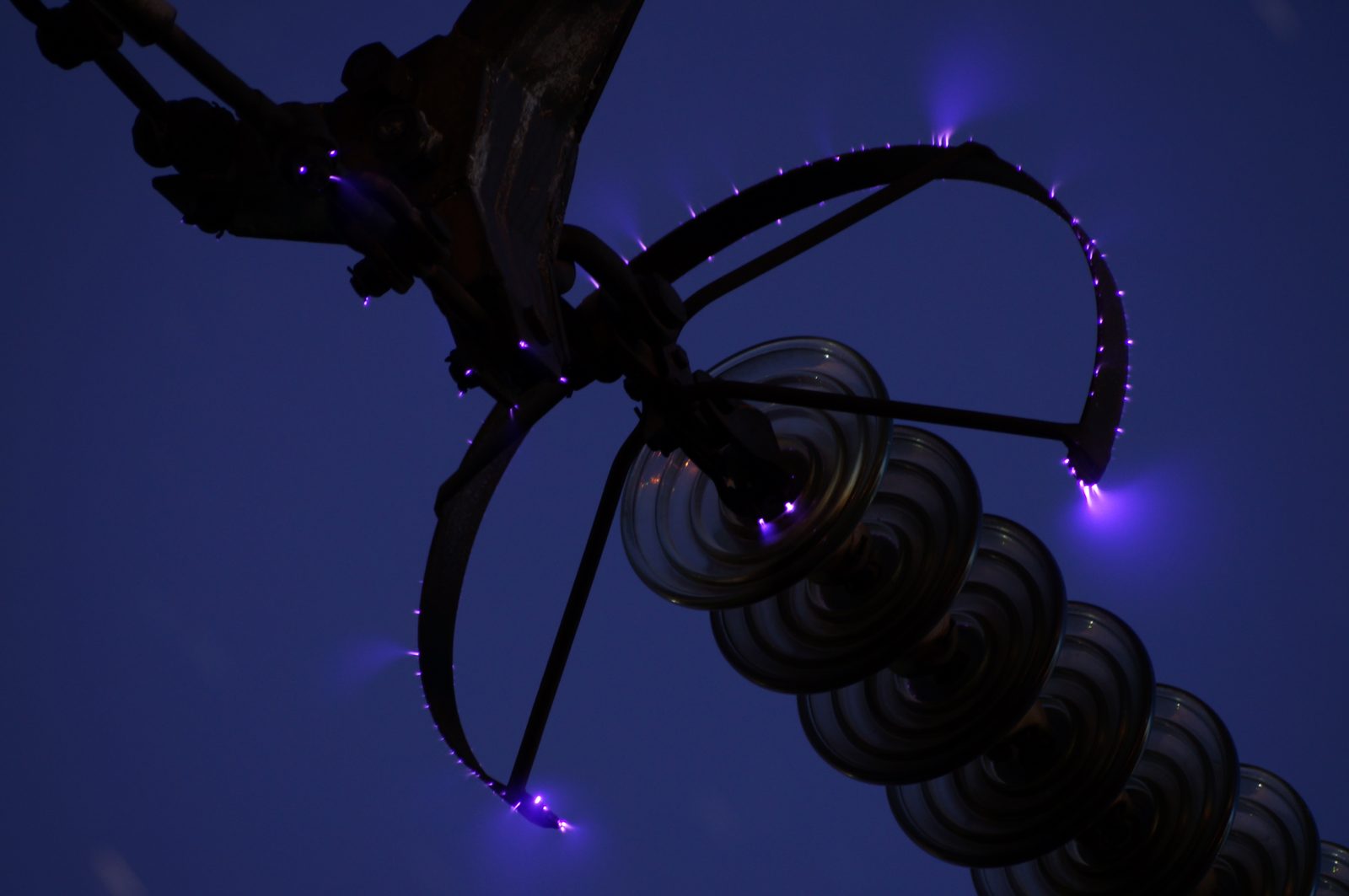 Corona discharge glowing on live line hardware at dusk