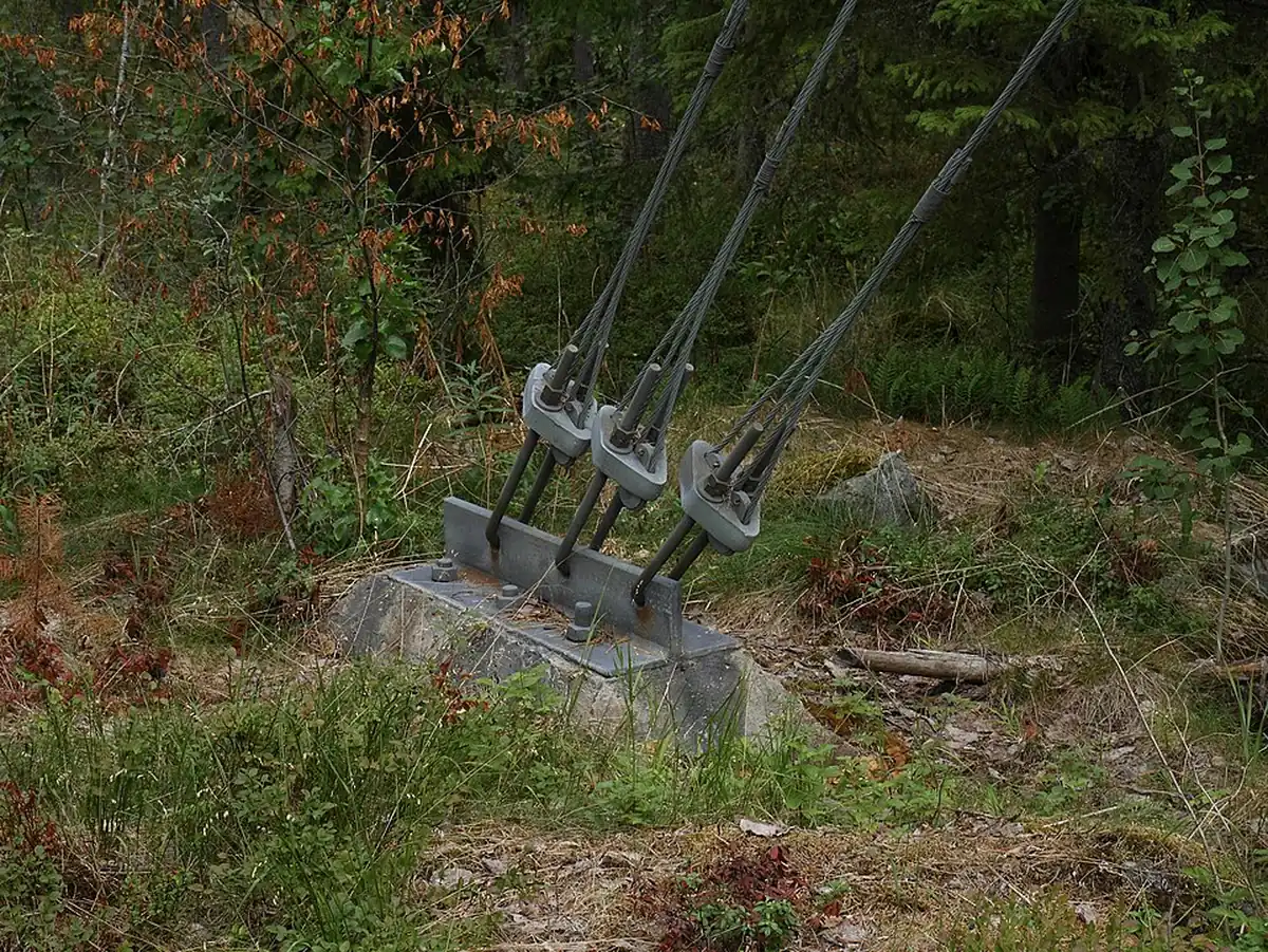 Guy anchor rods fixed to a concrete deadman block in wooded terrain