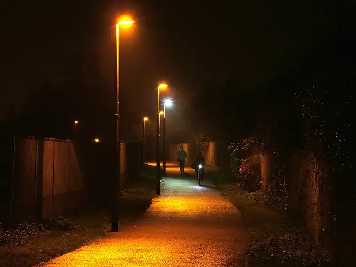 Streetlight luminaires on pole brackets lighting a footpath at night