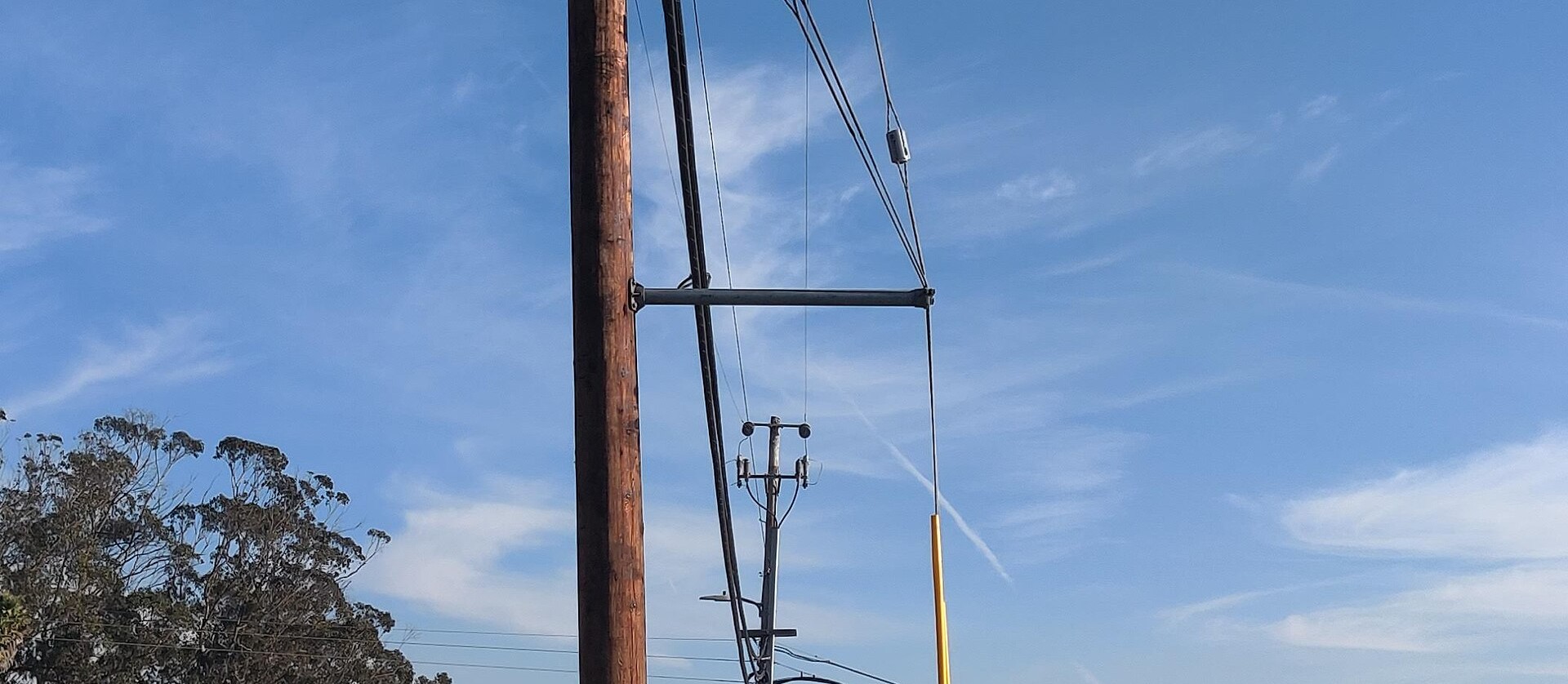 Guy wire anchored to a wood distribution pole beside a sidewalk guy guard