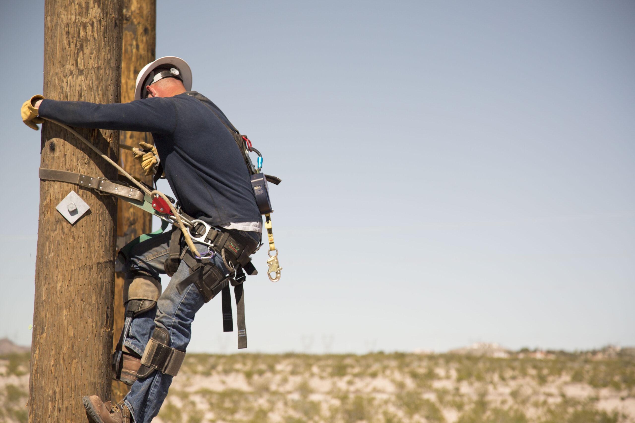 Lineman in safety harness climbing a wooden utility pole to work on pole hardware