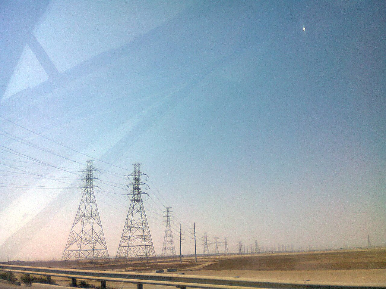 Transmission towers crossing desert terrain under a dust-hazed sky