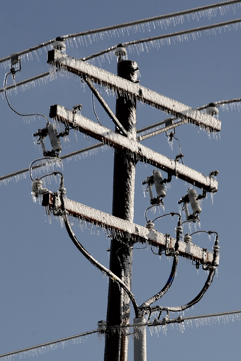 Distribution pole with iced cross-arms and pin insulators carrying long icicles after freezing rain