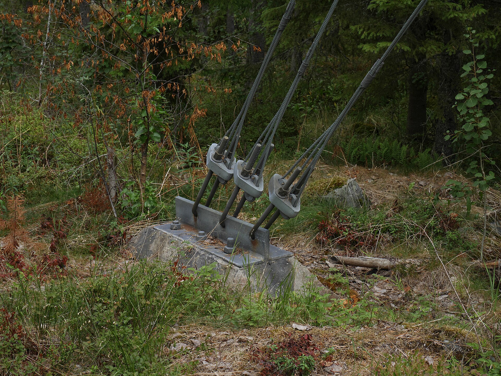 Three guy wire anchor assemblies with eye-end rods at a mast base