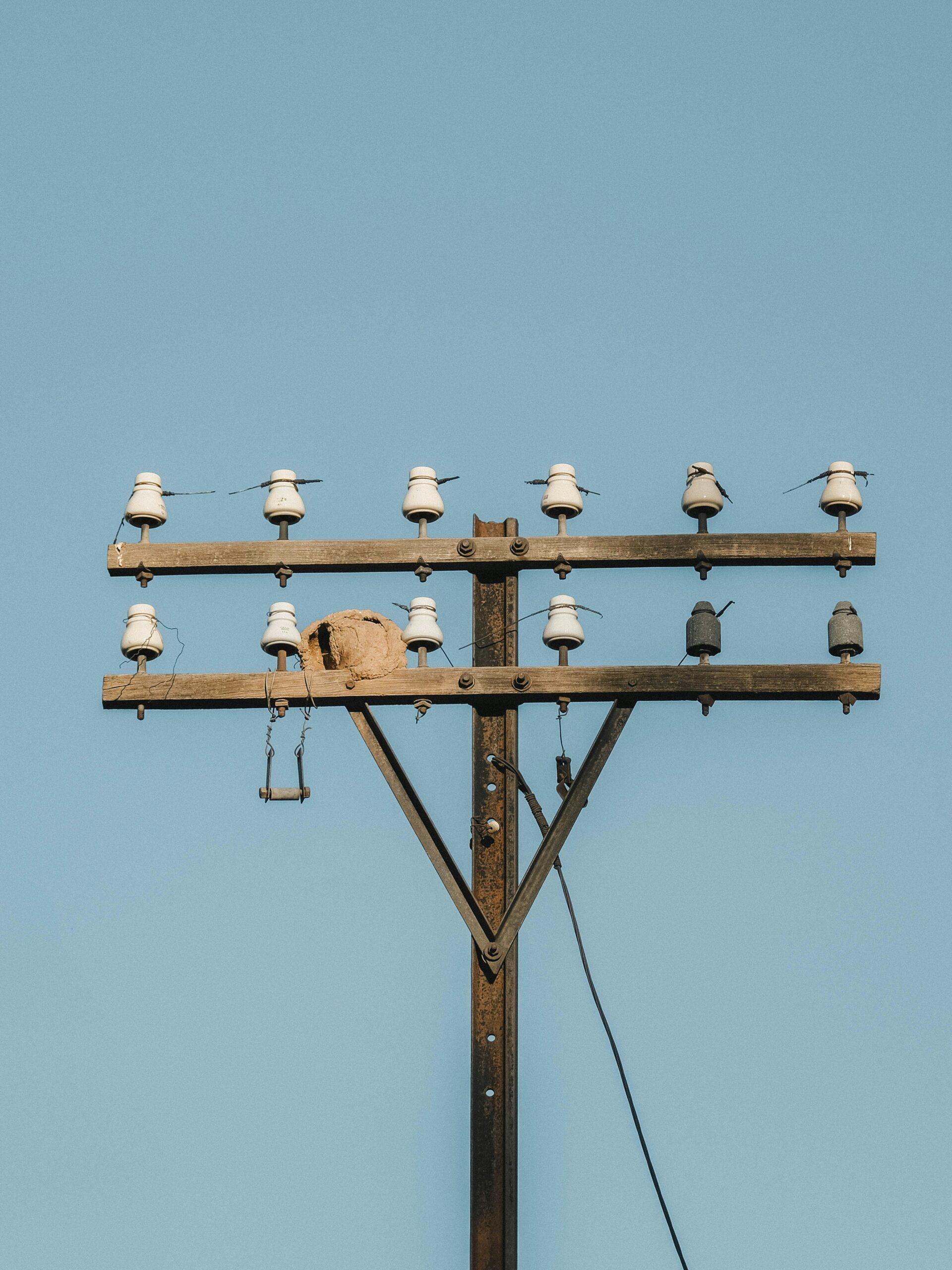 Wooden telephone pole with ceramic insulators against blue sky